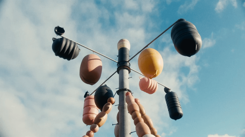 a gif of a kinetic, spinning installation on a pole with numerous plastic buoys and fishing floaters hanging from it