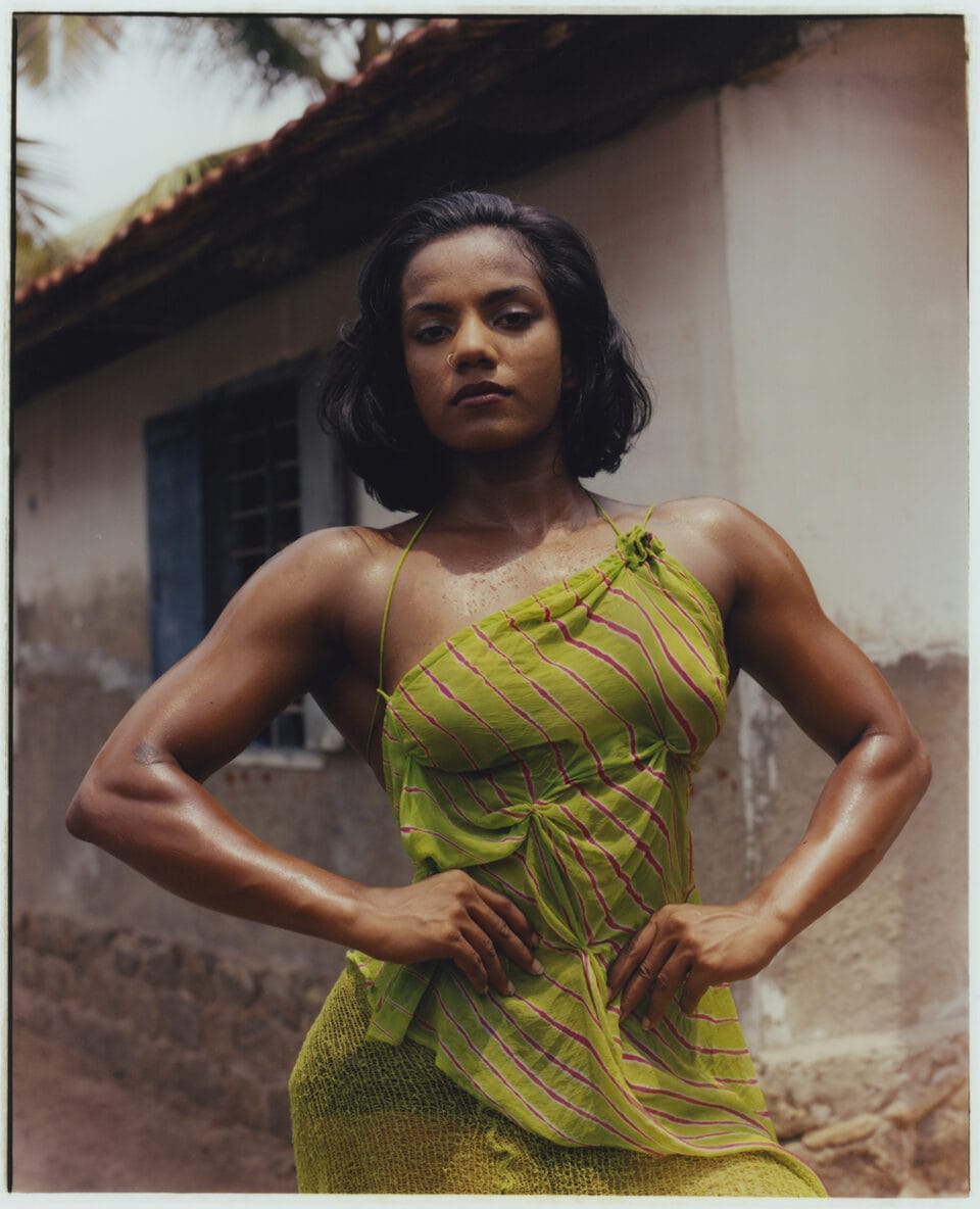 an indian woman in a green dress with large muscles stands wiht her hands on her hips