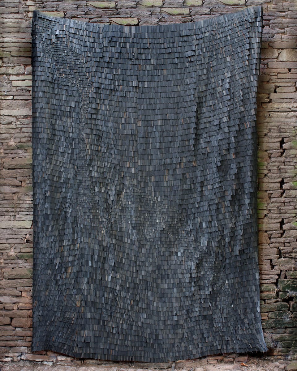 a hanging tapestry-like artwork made of tiny, dark, wooden shingles